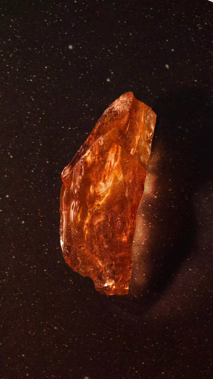 Translucent amber resin fragment with golden shimmer against a dark background with fine sparkles.